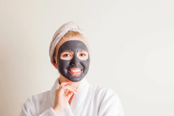Śmiejąca się młoda dziewczyna z ręcznikiem na głowie używając czarnej maski na twarzy — Zdjęcie stockowe