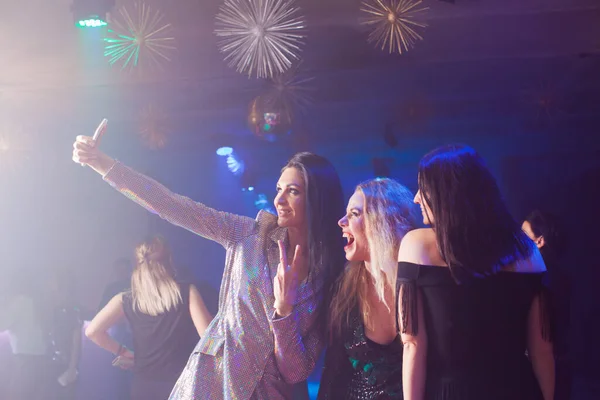 Emocionadas mujeres felices se están tomando una selfie juntas en un club nocturno usando un teléfono inteligente —  Fotos de Stock