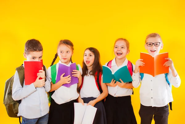 Heureux heureux heureux souriants petits étudiants tenant des livres de couleur isolés sur fond jaune. Retour à l'école. — Photo