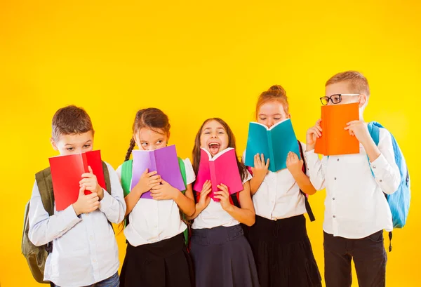 Heureux écoliers debout avec des livres colorés isolés sur fond jaune. Des enfants cachés derrière des livres — Photo