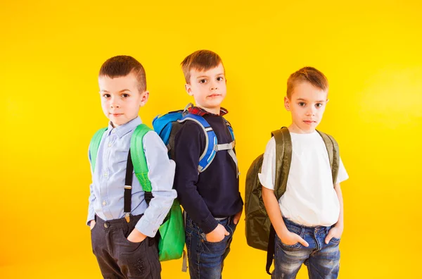 Leuke schooljongens in uniform met rugzakken op gele achtergrond — Stockfoto