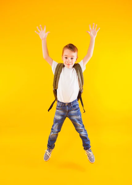 Glückliches Kind springt mit Rucksack über gelbem Grund zurück zur Schule — Stockfoto