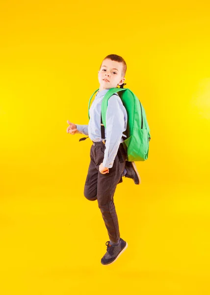 Foto eines kleinen Schülers, der hoch springt. glücklicher Schüler mit Rucksack isoliert auf gelbem Hintergrund. — Stockfoto