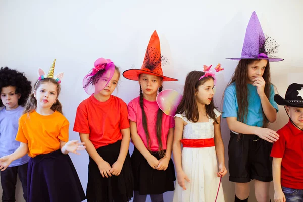 Un grupo de niños aburridos en una fiesta de cumpleaños. Niños con disfraces divertidos y sombreros con mal humor —  Fotos de Stock