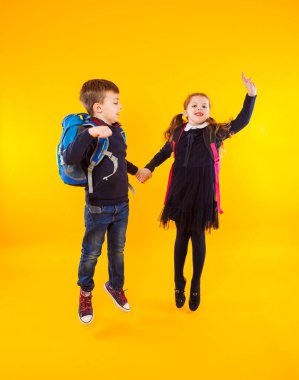 Schoolgirl and schoolboy jumping high over yellow