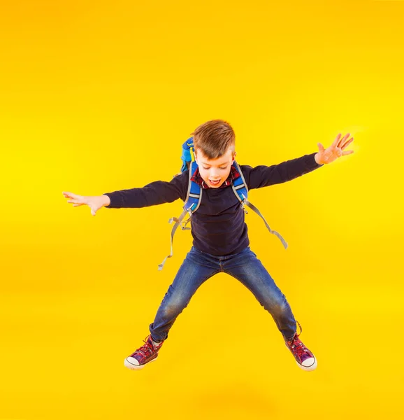 Happy kid jump with hand up. Cute exciting child boy ready to study with backpack isolated on yellow — 스톡 사진