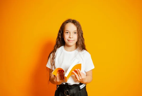 Pretty schoolgirl girl holding open book isolated on yellow — ストック写真