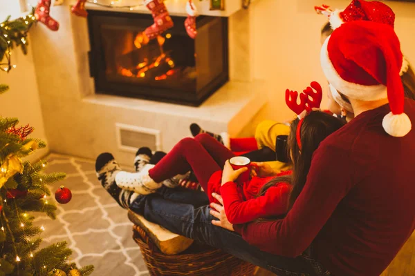 Fröhliche Familie in Weihnachtsmänteln trinkt Tee am Kamin — Stockfoto