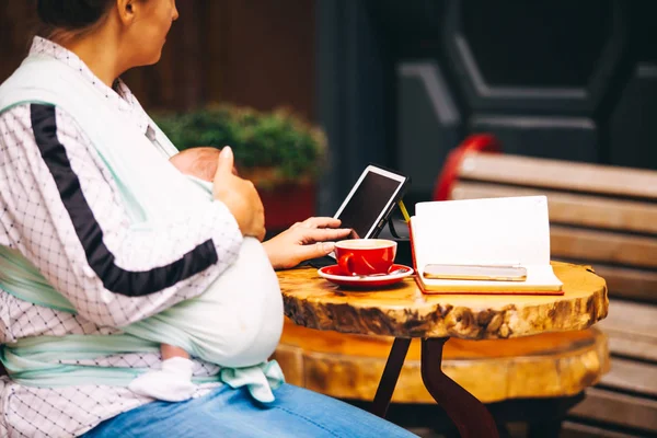 Young mother with her newborn baby working or studying with tablet — Stock Photo, Image