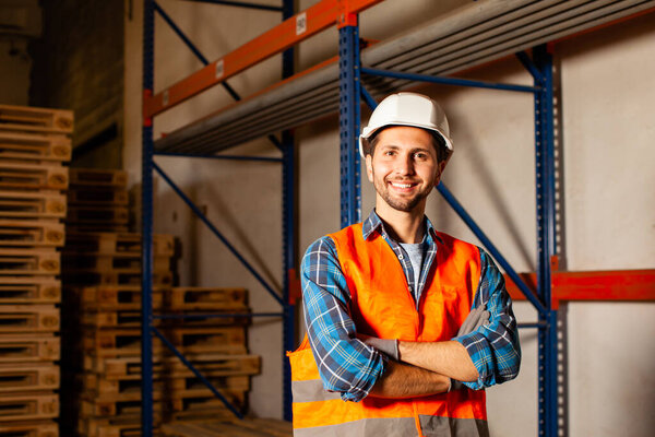 Confident handsome worker in protective hardhat and uniform at the warehouse of a industrial manufacturing