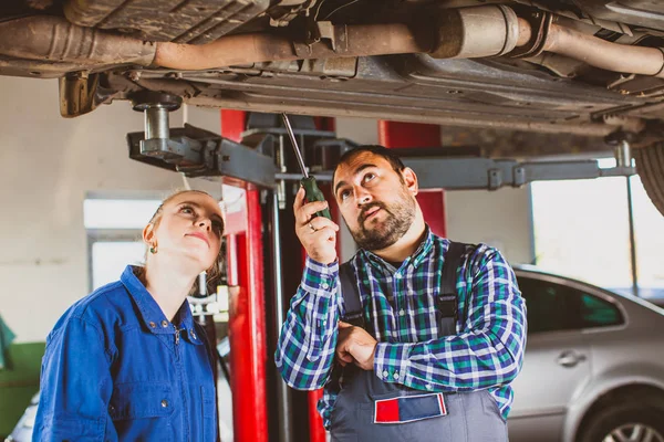 Mecánico hombre examinando coche con aprendiz chica — Foto de Stock