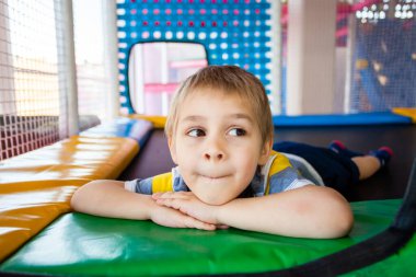 Küçük çocuk oyun merkezinde trambolinde dinleniyor.