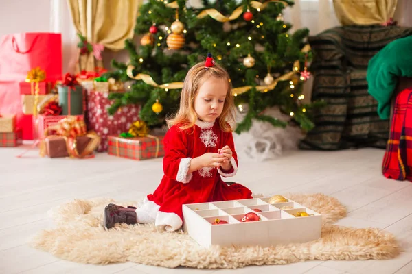 Söt liten flicka dekorera en julgran med färgglada grannlåt hemma — Stockfoto