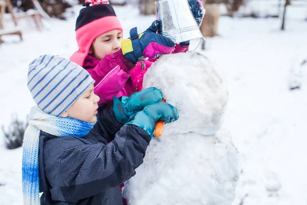 Des enfants heureux faisant un bonhomme de neige ensemble dans un parc d'hiver après une chute de neige — Photo
