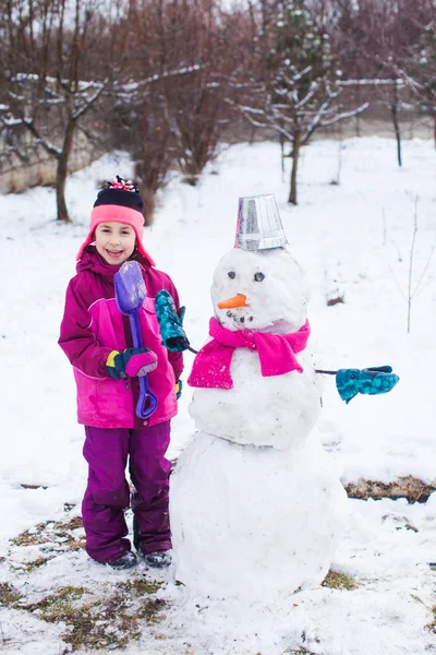 Mooi klein meisje in warm outwear gemaakt sneeuwpop in koude ijzige dag — Stockfoto