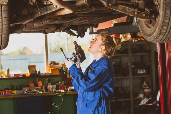 Молодая женщина-механик работает под машиной — стоковое фото