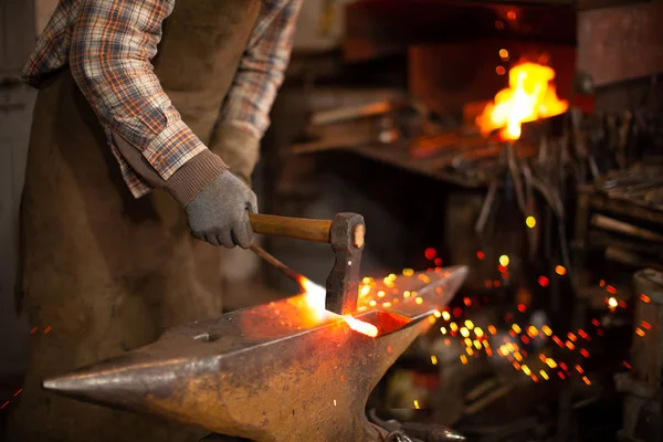 Herrero forjando manualmente el metal caliente en el yunque en herrería con fuegos artificiales de chispa — Foto de Stock