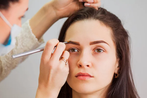 Master make-up corrigeert en geeft vorm aan wenkbrauwen in een schoonheidssalon — Stockfoto