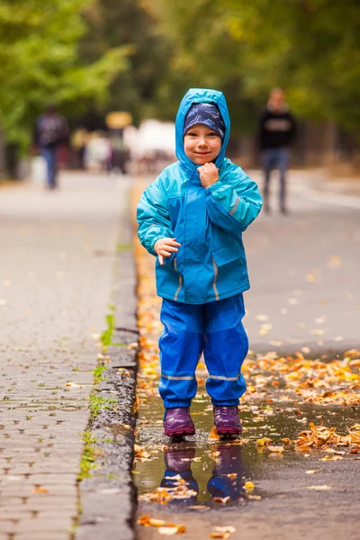 Le garçon se réjouit dans la flaque dans le parc d'automne — Photo