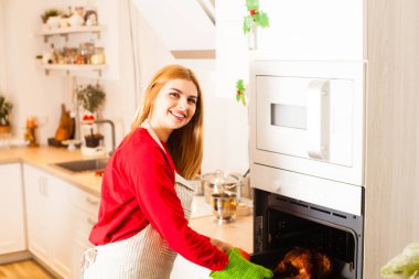 Woman in kitchen near oven holding plate with chicken