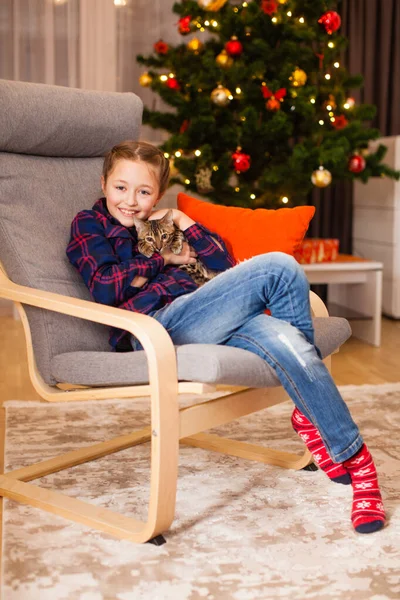 Κοριτσάκι που παίζει με χαριτωμένο γατάκι κοντά στο χριστουγεννιάτικο δέντρο — Φωτογραφία Αρχείου