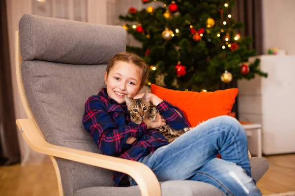 Χαμογελαστή κοπέλα αγκαλιάζει τη νέα της γάτα κοντά στο χριστουγεννιάτικο δέντρο — Φωτογραφία Αρχείου