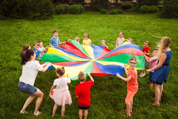 Kinder spielen mit Regenbogen-Fallschirm im Park — Stockfoto