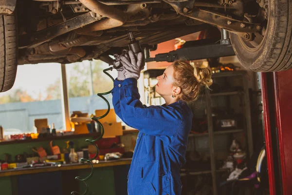 Mujer trabajando como mecánico de coche bajo coche levantado — Foto de Stock