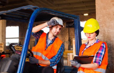 Warehouse manager checking order list. People in protective helmet, vest and gloves at factory.