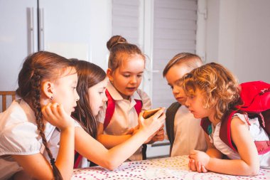 Cute pupils talking and using smartphone during break. Happy friends having fun together