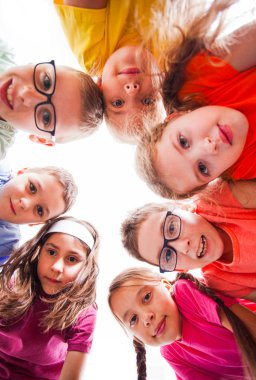 Cute boys and pretty girls looking at camera, view from down. Team of kids outdoors.