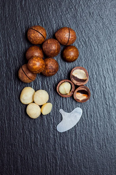 Macadamia-Nüsse mit Putzschlüssel liegen auf einer schwarzen Schiefertafel. Ansicht von oben, Kopierraum. — Stockfoto