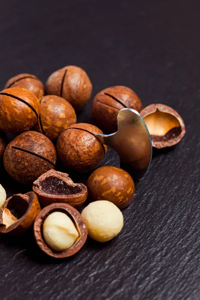 Whole and open macadamia nuts with key on black background. — Stockfoto