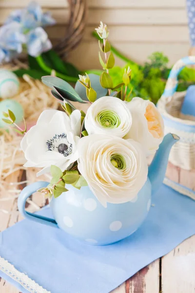 Bouquet of ranunkula in blue teapot on wooden surface — Stok fotoğraf