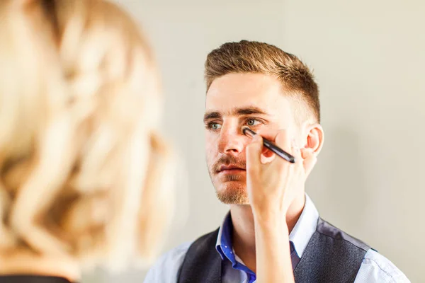 Knappe man doen make-up voor mode fotografie studio. — Stockfoto