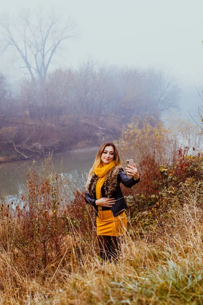 Sorrindo menina elegante fazendo selfie na natureza outono perto do lago . — Fotografia de Stock