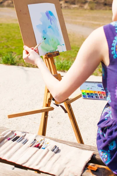 Girl is painting with watercolor on the easel outdoors. Spring imagination.