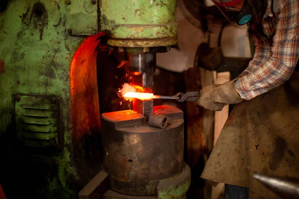 Herrero en guantes de seguridad poniendo metal calentado bajo la prensa mientras trabaja con la máquina de prensa metalúrgica. — Foto de Stock