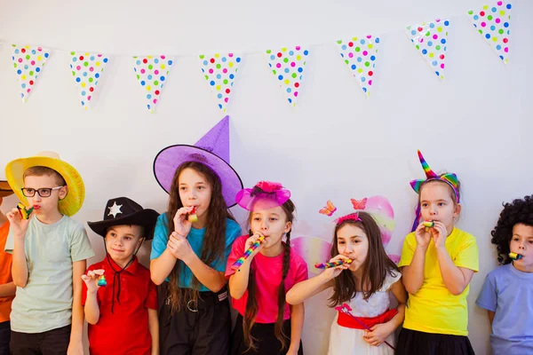 Χαρούμενα χαρούμενα παιδιά γιορτάζουν τα γενέθλια τους και φοράνε αστεία καπελάκια. Χαριτωμένα παιδιά σφυρίζουν — Φωτογραφία Αρχείου