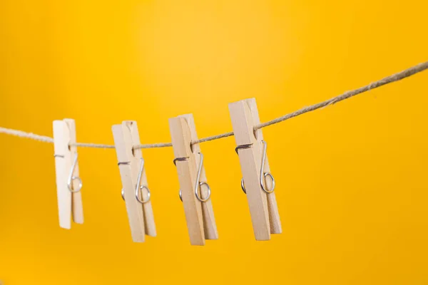 Wäscheklammern aus Holz hängen an einem Seil über gelbem Hintergrund. — Stockfoto