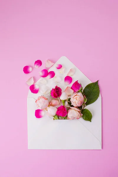 Greeting card with open envelope and pink tea rose flowers. Rose petals fly out of paper envelope. — Stok fotoğraf