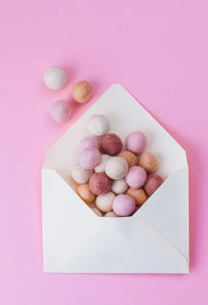 Минимальная композиция с войлочными шариками, вылетающими из открытого конверта на розовом фоне — стоковое фото