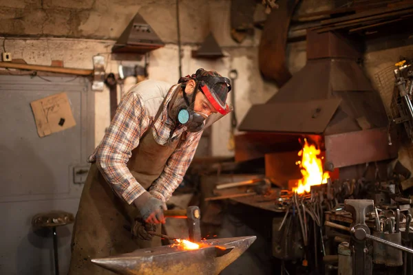The blacksmith forging the molten metal on the anvil in smithy. — Stock Photo, Image