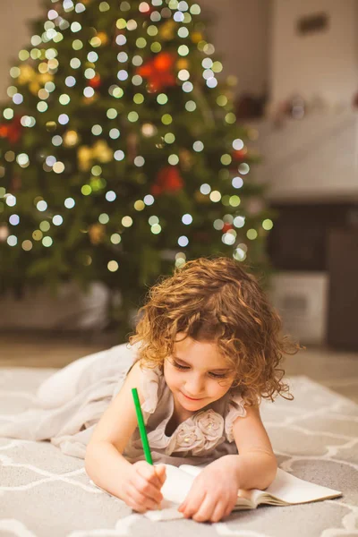 Christmas holidays and childhood concept with girl, writing on a floor