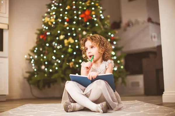 Dreamy girl sitting near decorated Christmas tree — 图库照片