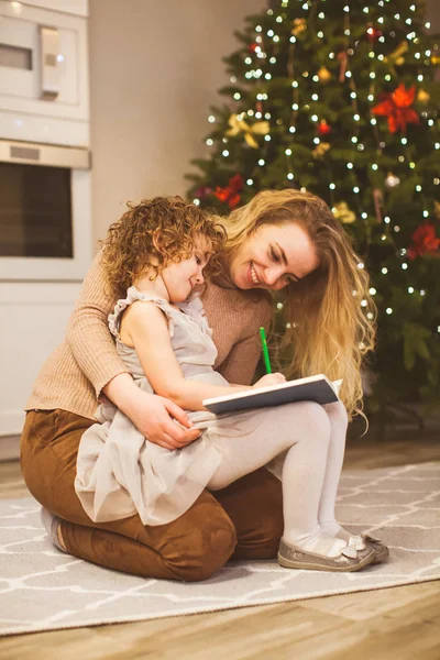 Mother holding her daughter on knees near Christmas tree — Stockfoto