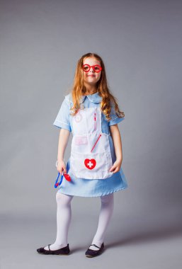 Doktor kostümü giymiş küçük bir kız gri arka planda izole edilmiş..