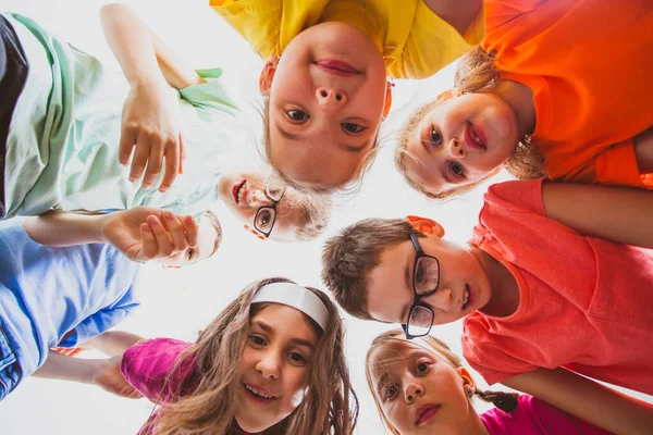 Team van lachende kinderen omhelzen elkaar in een cirkel, uitzicht vanaf beneden. — Stockfoto