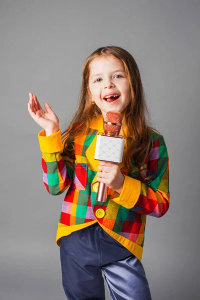 Маленька співачка. Маленька дівчинка з мікрофоном на сірому фоні . — стокове фото