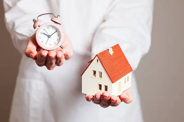 Woman holding alarm clock and mockup house — Stock Photo, Image